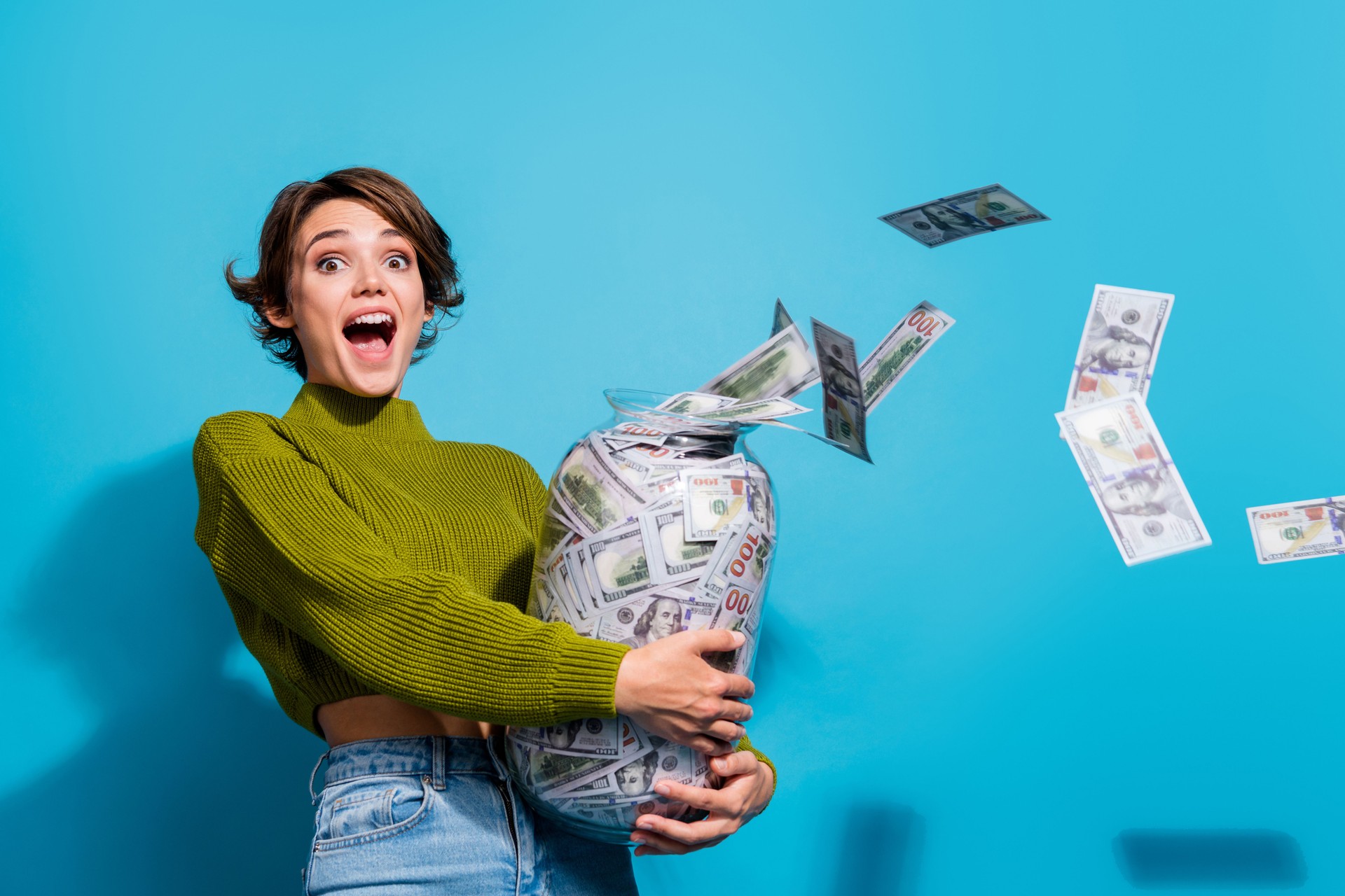 Foto von glänzender positiver Dame trägt grünen Pullover mit schwerem Bargeld Ersparnisse Glas isoliert cyan Farbe Hintergrund